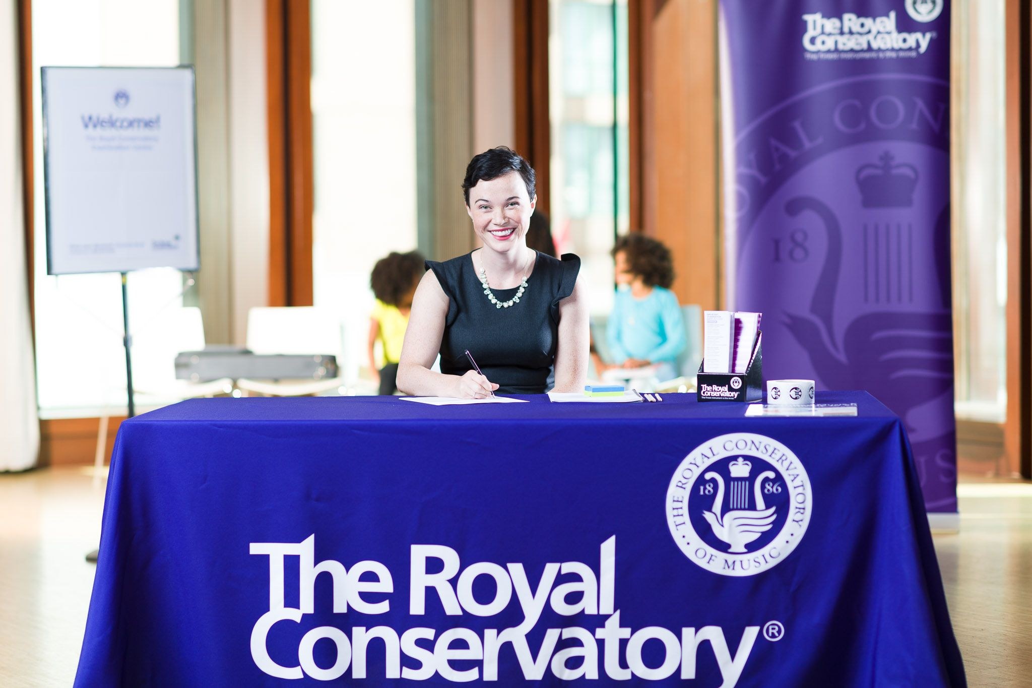 woman smiling while sitting in front of a table covered with cloth that has royal conservatory logo and print